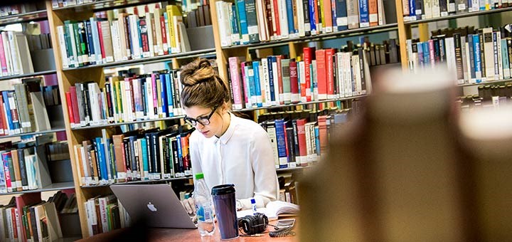 En kvinna studerar i en biblioteksmiljö.