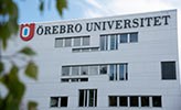 White building with a sign saying Örebro University. There are green leaves in the foreground.