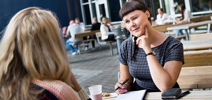 Två studenter fikar och samtalar vid ett bord.