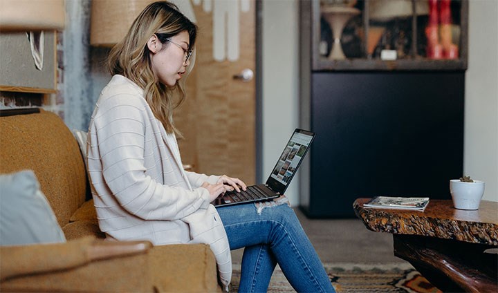 Kvinna sitter i soffa med laptop i knäet