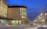 Universitetsbiblioteket i kvällsljus med snö på marken.