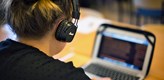 Foto på student som sitter med hörlurar vid en dator.