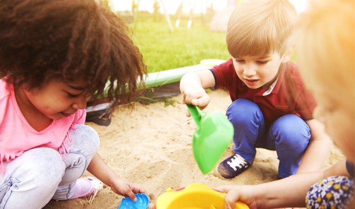 Children playing in a sandpit with buckets and spades.