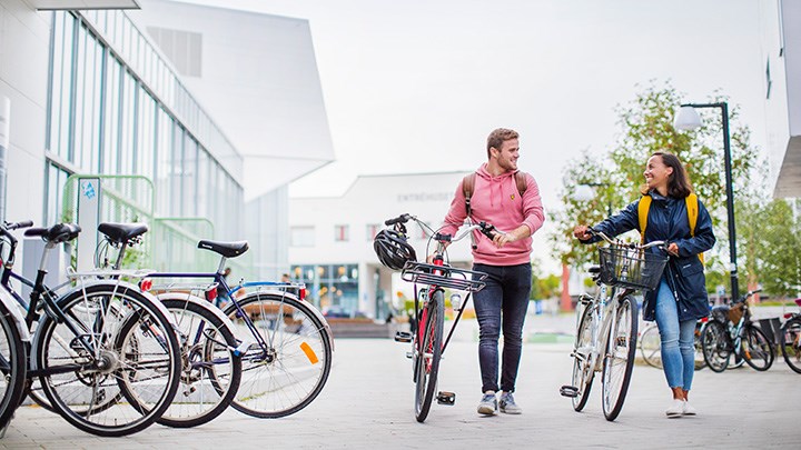 Två studenter går med sina cyklar ute på campus.