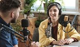Foto på två personer som sitter i en radiostudio med mikrofoner intill sig.