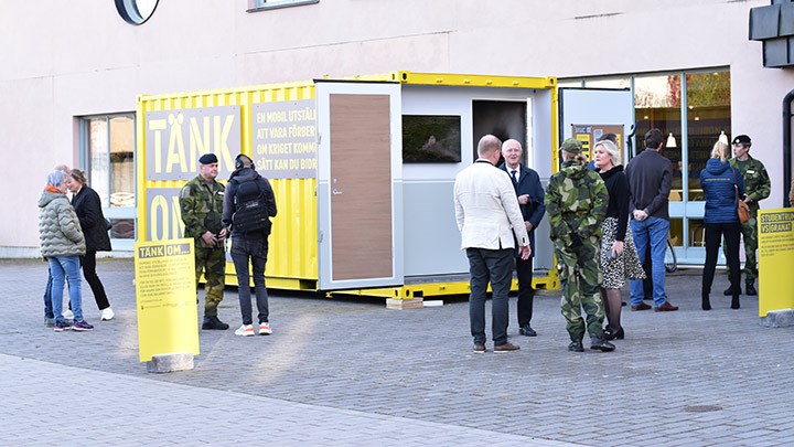 Människor framför en gul container. En del av persoenrna har militär uniform.
