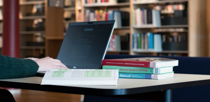 Photo of a person sitting by a table with a laptop and four books.