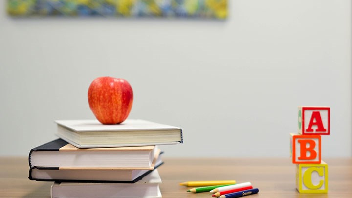 Bord med böcker, pennor, bokstavskuber och ett äpple som symboliserar kunskap i skolan