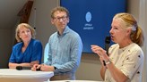 Två kvinnor och en man i samtal vid ståbord. En av kvinnorna har en mikrofon i handen. 