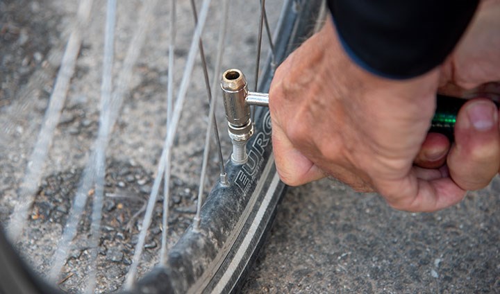 Närbild på pumpning av cykel. Vi ser ett däck och ett par händer som håller i munstycket till en en pump.