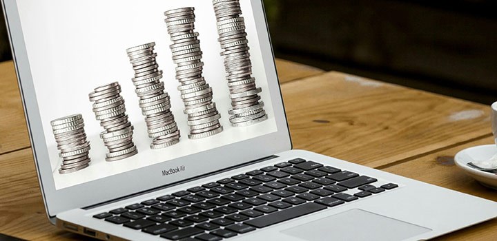 A laptop is on a table. The display shows stacks of coins.