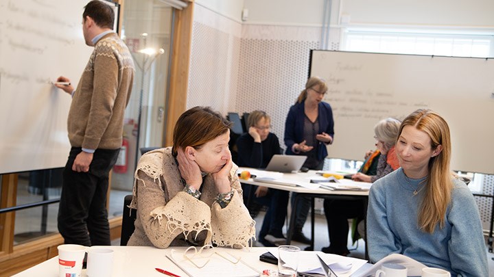 Helen Gustafsson och Elin Vimefalll diskuterar vid ett bord. Joakim Norgerg skriver på en whiteboard.