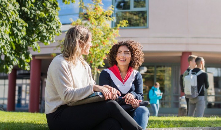 Två kvinnliga studenter som sitter utomhus och samtalar vid biblioteket