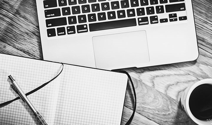 Writingbook, pen, computer, coffecup. The picture is black and white.