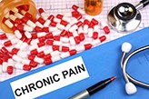 Pills in red and white, a stethoscope, a pen and the word 'chronic pain'.