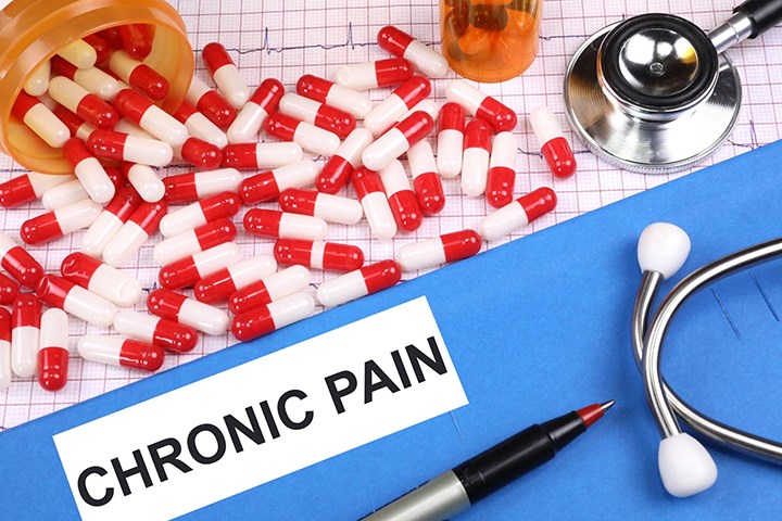 Pills in red and white, a stethoscope, a pen and the word 'chronic pain'.