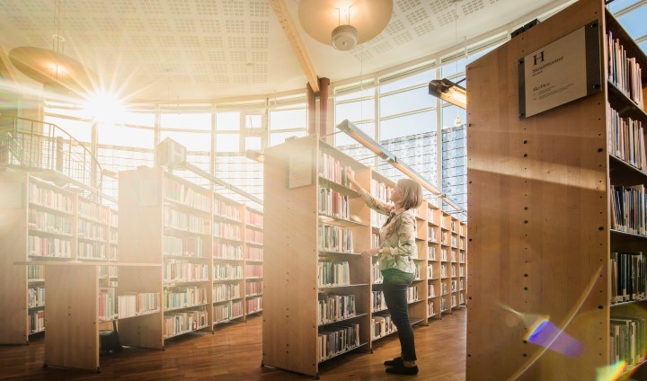 Bibliotek med tre hyllor och en tjej med solljus genom fönstren