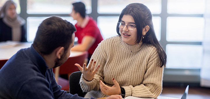 Två studenter som sitter och pratar med varandra.