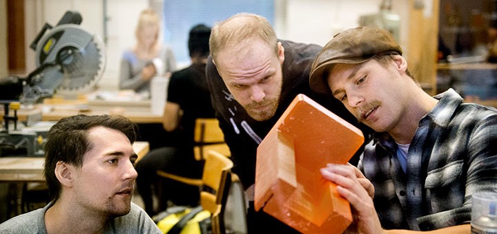 Three men closely studying an orange-coloured object.