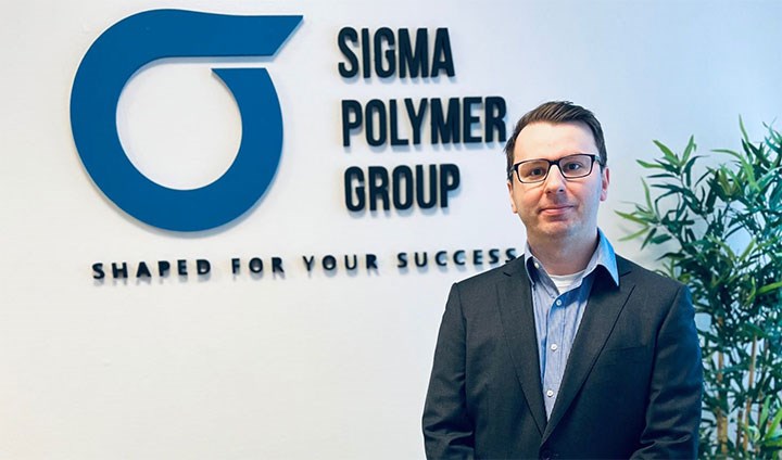 Deniz Muharemi framför Sigma Polymer Groups logotyp.