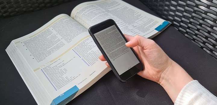 A hand holding a mobile phone showing text, over a textbook.