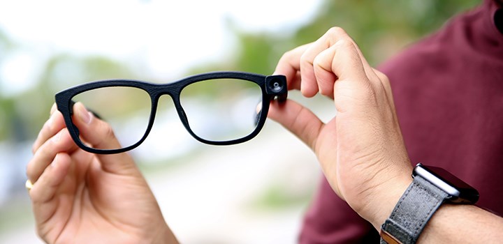 Photo of two hands showing a pair of glasses with a built-in camera.