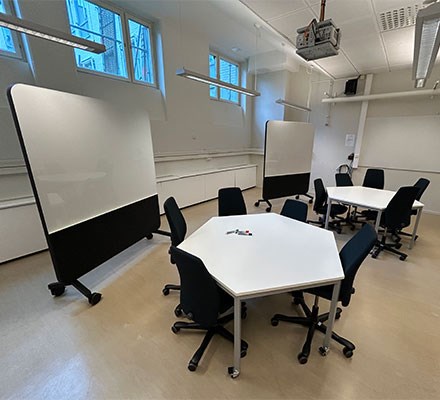 Vy 2 - Sexkantiga bord med stolar framför en rullbar whiteboardtavla