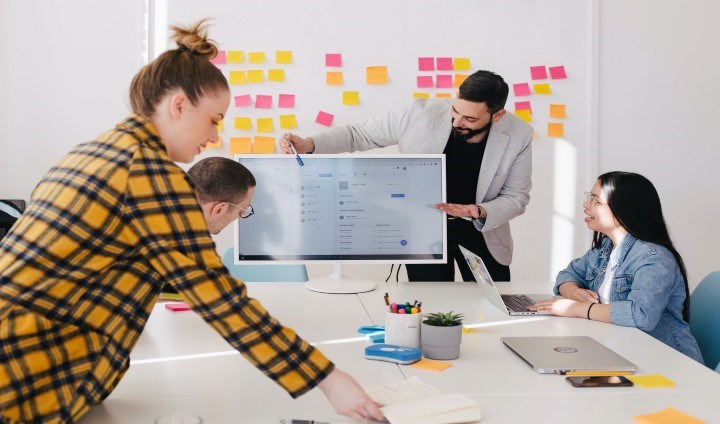 Fyra personer i arbetsmöte med post-it-lappar på whiteboard och datorskärm på bordet