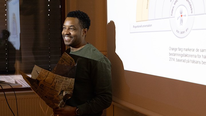 Adrian Hosford-Donovan with flowers in front of a white screen with a PowerPoint presentation.