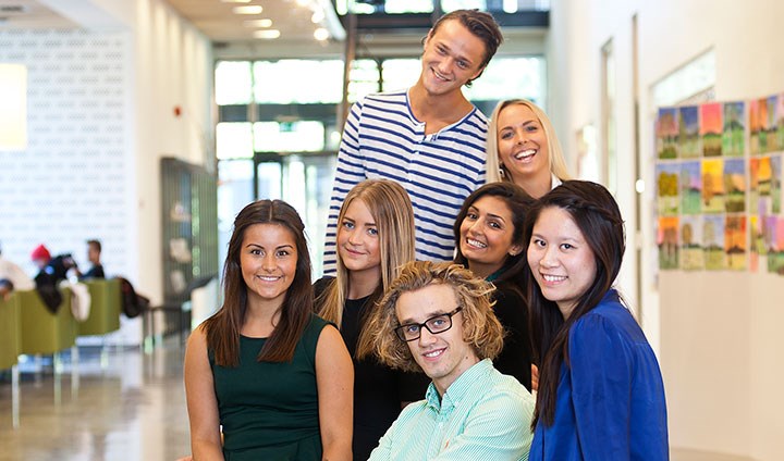 Sju glada studenter ler tillsammans i grupp.