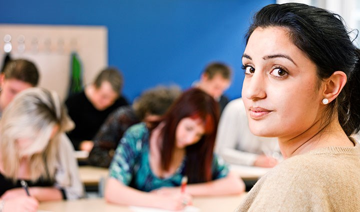 Female teacher looking into the camera. She is sitting in front of students.