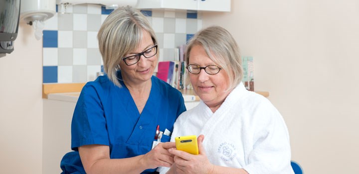 A nurse and a patient are looking at an mobile phone.