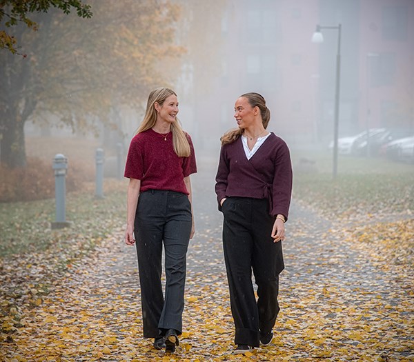Elin Vimefall and Ebba Löfgren are walking along a street. It is autumn, with yellow leaves on the road and fog.