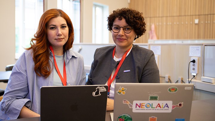 Two women are sitting at a table with their own laptops.