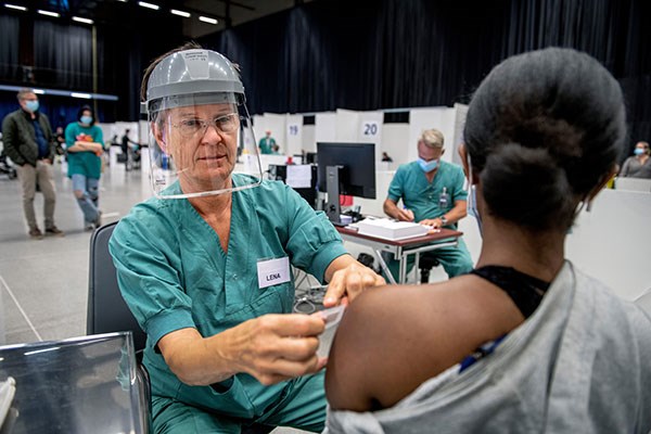 A woman getting a vaccine jab by a nurse wearing a face shield.