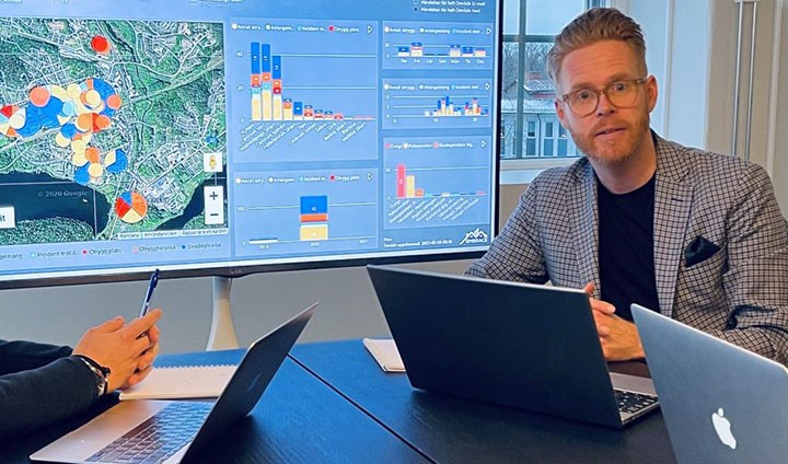 Henrik Andershed sitter vid en laptop. I bakgrunden syns en kartbild med röda markeringar över vissa områden.