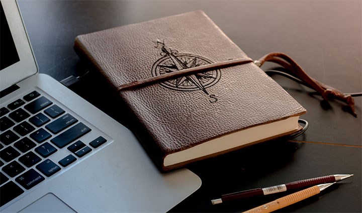 Läderbok med en kompass som ligger på en öppen laptop