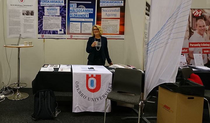 Maria Holmström fanns på plats för att berätta om universitetets äldreforskning. På bilden står hon bakom ett bord draperat med universitetets flagga och i bakgrunden syns posters.