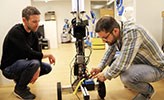 Two men kneeling in front of a robot.