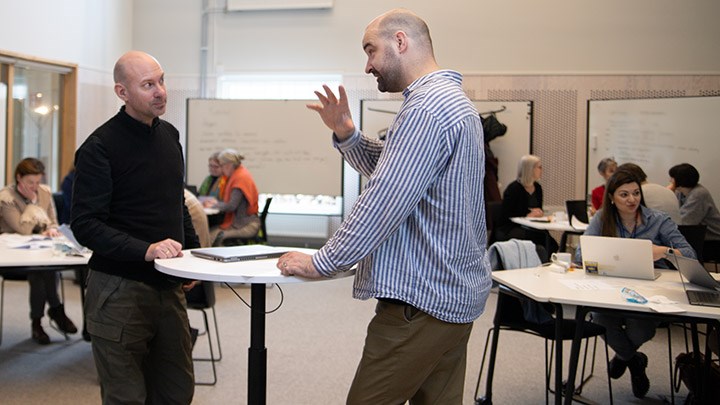 Henric Bagerius och Eric Borgström diskuterar framför lärare som grupparbetar. 