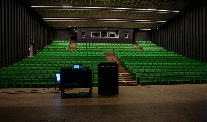 Massor av tomma gröna stolar i den stora Aula Nova. I förgrunden syns en öde scen och en tom talarstol.