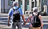 Två seniora personer, ses bakifrån, promenera i stadsmiljö.