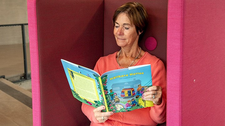 Bibbi Larsliden läser i sin bok Hållbara hatten. Hon sitter i en ljusröd fåtölj.