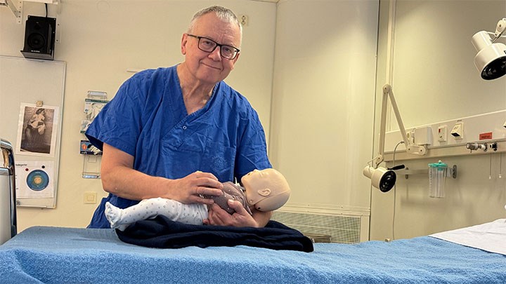 Mats Eriksson i sjuksköterskekläder håller en docka i träningsmiljön Kliniskt träningscenter vid Örebro universitet.