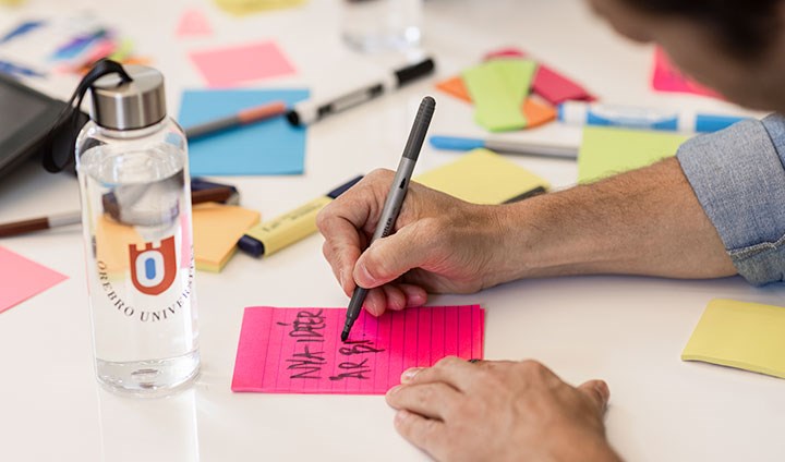 A table with notes with colorful notes. A hand writes on one of them.