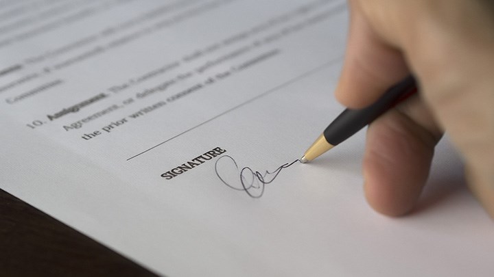 Foto på en hand som skriver under att pappersavtal.