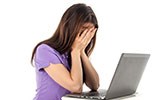 A woman hides her face in her hands at a computer.