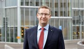 En person med slips och kavaj som står utomhus framför fönstren av Novahuset.