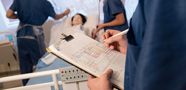 A person is taking notes by a hospital bed.