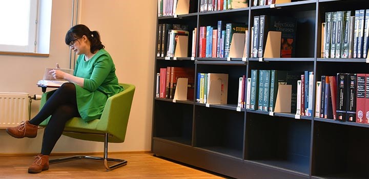 Kvinna sitter och läser en bok i ett bibliotek